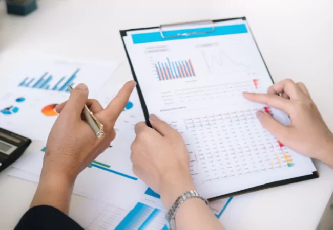 A close-up of hands holding a pen and pointing at a graph