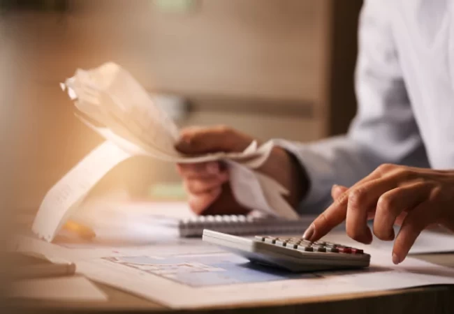 A person is calculating expenses or managing finances with a calculator and receipts on a desk