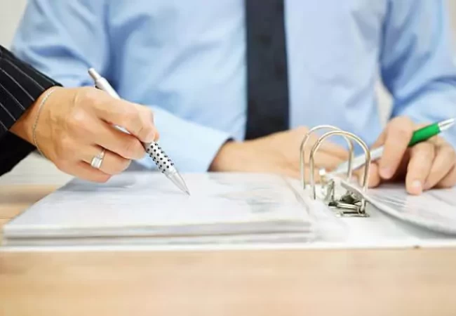 A person holding a pen and writing on a binder